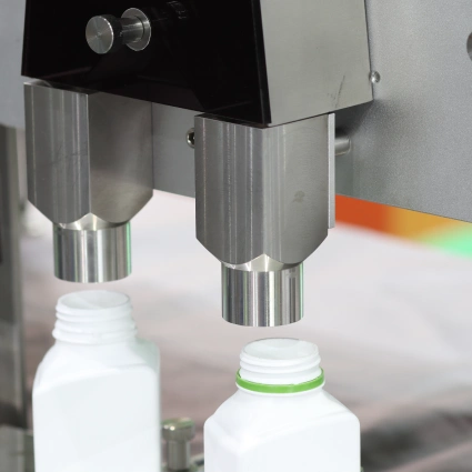 Máquina automatizada colocando tapas en botellas plásticas dentro de línea de envasado para cosmética