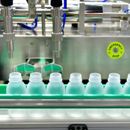 Cabezal dosificador llenando botellas con productos líquidos en línea de producción cosmética