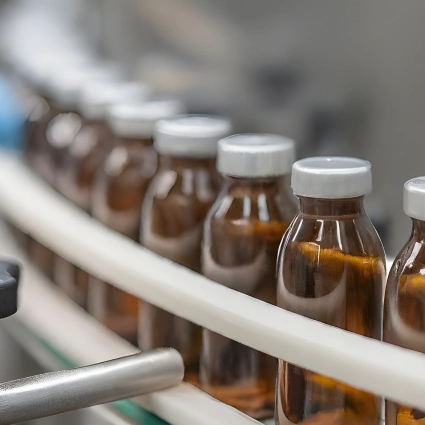 Línea de producción con viales marrones de vidrio en cinta transportadora en entorno farmacéutico